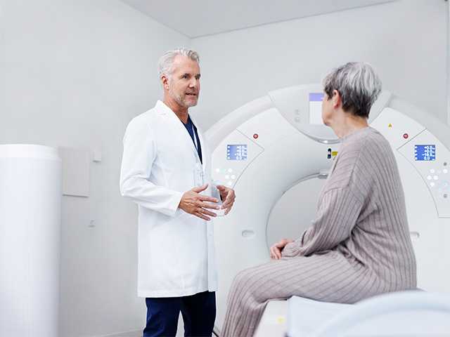 Corewell Health nuclear medicine imaging specialist speaks with a patient as she sits in front of an imaging system