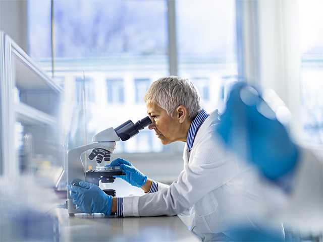 Female doctor in white lab coat looks into a microscope