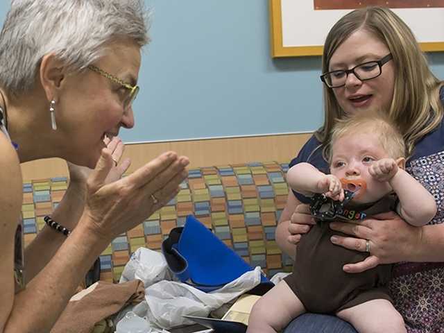 Mom holds baby in her lap while doctor plays peek-a-boo in neurofibromatosis clinic