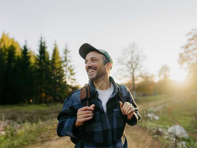 Smiling middle aged white man stands in the evening sun while hiking outdoors