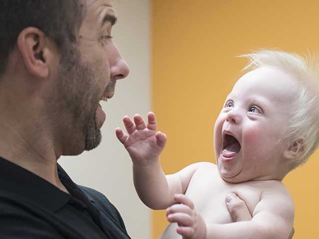 Smiling man holds a smiling baby boy in the neurodevelopmental pediatrics clinic