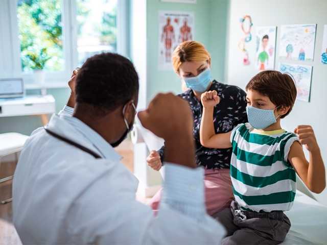 Young boy flexes his arms alongside doctor