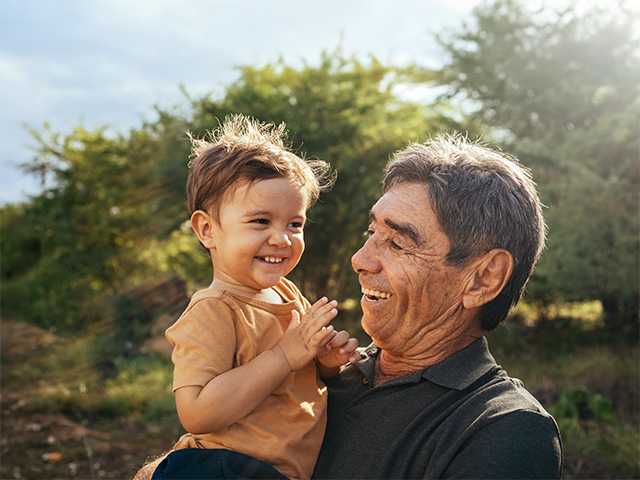 Older man holding a young boy while outside smiling 
