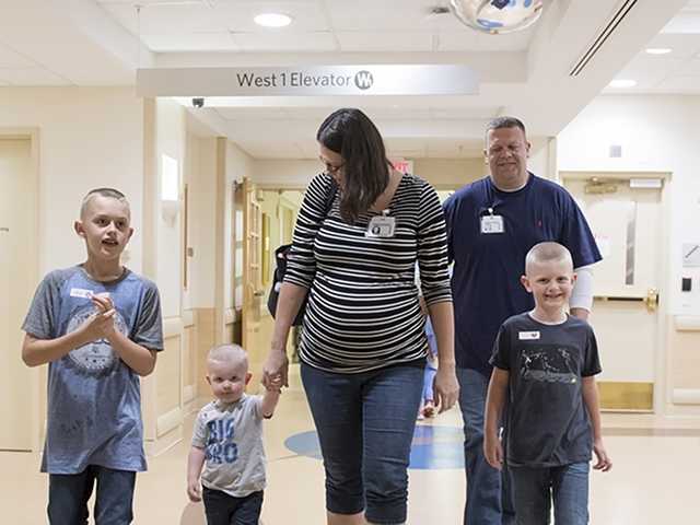 Mother and father and their three sons walk into the neonatal intensive care unit for a visit