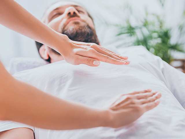 Man lies down on his back with eyes closed while receiving reiki therapy